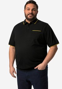 Svart pikétröja med gula accenter på kragen och fickan. Korta ärmar, en bröstficka, tillverkad av lättviktig tyg.