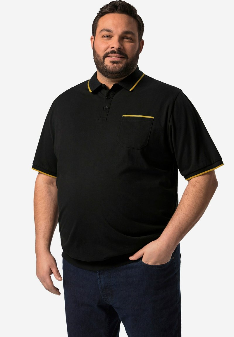 Svart pikétröja med gula accenter på kragen och fickan. Korta ärmar, en bröstficka, tillverkad av lättviktig tyg.