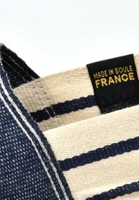 Sac en toile avec motif rayé bleu marine et crème. L'étiquette en tissu indique "FABRIQUÉ À SOULE, FRANCE." Présente des bords cousus et une texture durable.