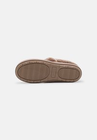 Pantoufle en fausse fourrure marron avec une semelle en caoutchouc texturée, présente un motif en côtes horizontal et une légère élévation au niveau du talon.