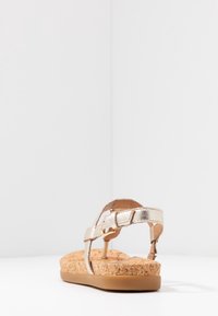 Kultaiset metalliset remmisandaalit, joissa on korkkipohja, litteat kumipohjat ja säädettävä nilkkaremmi, jossa on solkiyksityiskohta.