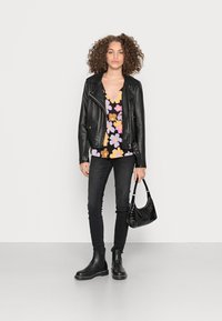 Jaqueta de motociclista em couro preto, blusa com padrão floral em preto, laranja e roxo; jeans skinny pretos, botas de tornozelo e uma pequena bolsa preta.