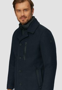 Marineblauer Wollmischmantel mit Reverskragen, doppelter Knopfleiste, Reißverschlusstasche und strukturiertem Stoff.