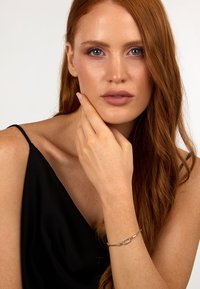 Silverarmband med ovala och rektangulära länkar, prytt med små ädelstenar. Modellen bär en svart ärmlös topp och har långt, vågigt rött hår.