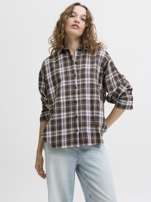 Brown and white checkered shirt with an oversized fit, button-down front, and rolled-up sleeves paired with light blue denim jeans.