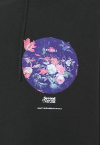 Tela negra con un diseño floral circular en púrpura y rosa, con el texto "Levi's", "Second Nature" y "La calidad nunca pasa de moda".