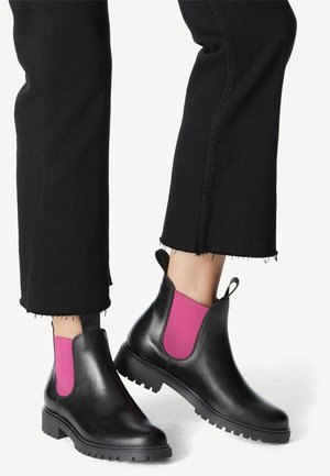 Bottes noires en cuir à la cheville avec des panneaux latéraux élastiques roses, surface texturée et semelle crantée ; portées avec un jean noir court à ourlets effilochés.
