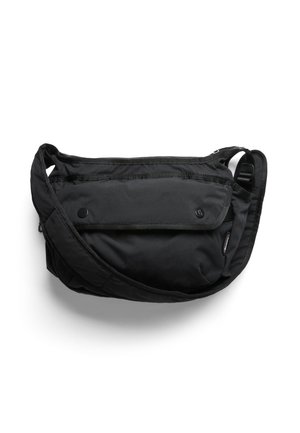 Sac bandoulière en tissu noir avec sangle réglable, poche avant à rabat sécurisée par deux boutons-pression, et compartiment principal zippé.