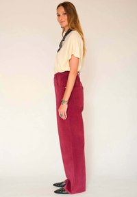 Haut crème à manches courtes, pantalon en velours côtelé bordeaux et chaussures noires à bouts pointus. Les accessoires incluent une écharpe à motifs et des bracelets.
