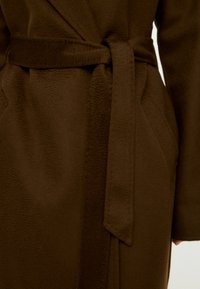 Brauner strukturierten Stoffbademantel mit einem gebundenen Gürtel in der Taille und Seitentaschen. Das Material wirkt weich und wird in einer Nahaufnahme präsentiert.