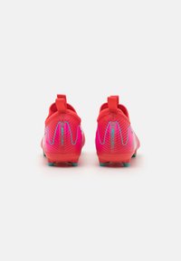 Bottines de football rouges avec une surface texturée, conçues avec un dégradé d'accents roses et bleus. Comprend une languette au niveau du talon pour un enfilage facile.