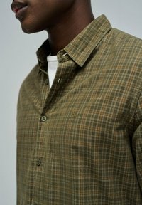 Koszula zapinana na guziki w kolorze oliwkowym w kratę, z wyprofilowanym kołnierzykiem, teksturowanym materiałem i logo na piersi.