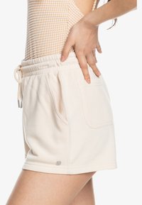 Cremfarbene, weiche Baumwollshorts mit elastischem Bund und verstellbarem Kordelzug. Mit Seitentaschen und einem kleinen Logodetail.