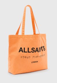 Orange canvas tote bag med svart "ALLSAINTS" text och ytterligare tecken, med två långa handtag och rektangulär form.