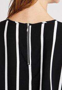 Nära bild av en person som bär ett svart plagg med vertikala vita ränder och en silvrig dragkedja vid nacklinjen baktill.