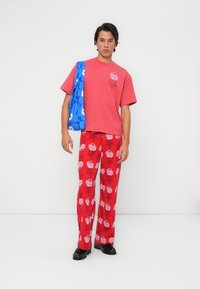 Pantalones de estampado floral rojo con rosas rosas, combinados con una camiseta rosa bordada con rosas. Accesorios: un bolso azul con estampado.