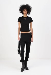 Svart tettsittende t-skjorte med rund hals og logoaccent. Kombinert med svarte joggebukser med hvite side-striper og ankelhøye støvler.