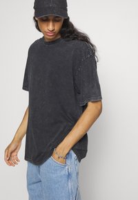 Sort oversized t-shirt med en falmet struktur, korte ærmer, rund halsudskæring og buet kant, parret med lyseblå jeans.