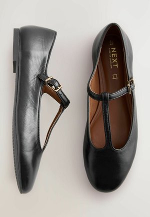 Ballerines Mary Jane en cuir noir avec un bout arrondi, une sangle ajustable et un design découpé. Texture lisse avec un talon bas et un intérieur marron.
