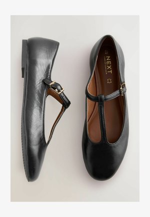 Ballerines Mary Jane en cuir noir avec un bout arrondi, une sangle ajustable et un design découpé. Texture lisse avec un talon bas et un intérieur marron.