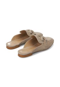 Mules de ante en beige claro, sin talón, con punta redondeada, detalle decorativo de nudo y un bajo tacón de madera. Plantilla de cuero lisa visible.