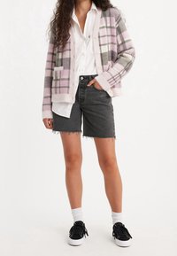 Cardigan de cuadros en tonos pastel rosa, gris y blanco, con un ajuste holgado y textura suave. Combinado con shorts de mezclilla negros y zapatillas negras.