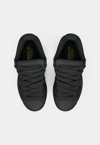 Czarne trampki z gumowym czubkiem, wyposażone w grube czarne sznurowadła i wyściełany język. Złote akcenty logo na wkładkach.