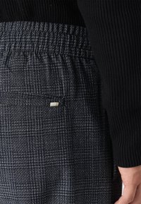 Pantalons tissés bleu foncé à motif à carreaux, dotés d'une taille élastique et d'une petite étiquette blanche sur la poche arrière.