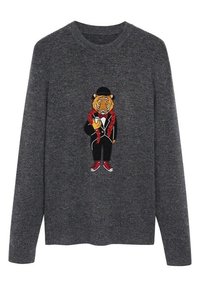 Un pull gris foncé avec un tigre brodé portant un smoking, des baskets rouges, un chapeau melons, un boa en plumes rouges et tenant un verre.