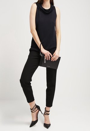 Top nero senza maniche con scollo drappeggiato, pantaloni neri su misura e tacchi alti neri con cinturini. Tiene una piccola borsa nera con nappina.