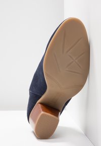 Scarpa in camoscio blu navy con tacco a blocco marrone; suola liscia con motivo antiscivolo testurizzato e design con punta arrotondata.