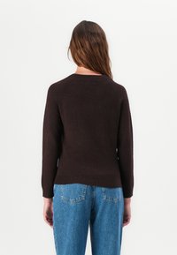 Brun strikket genser med lange ermer, rund halslinning og ribbestrikkede mansjetter, sammen med høyt liv lys blå denim jeans.