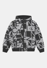 Chaqueta con capucha negra y gris con letras grandes mezcladas y logotipos "cK" impresos por todas partes, con cremallera en el frente y puños y dobladillo acanalados.