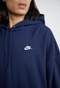 Μπλέ φούτερ από μαλακό ύφασμα, με kangaroo τσέπη και λευκό λογότυπο Nike στο στήθος. Κουκούλα με ρυθμιζόμενα κορδόνια.