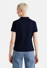 Námořnická modrá polo košile s krátkými rukávy, s límečkem a bočními rozparky, kombinovaná se světlými modrými džíny s vysokým pasem.