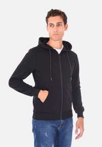 Felpa nera con zip e cappuccio regolabile, tasche frontali e polsini a coste. Realizzata in un tessuto morbido con una superficie liscia.