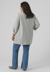 Pull long gris avec une coupe décontractée, doté de poignets roulés, porté sur un jean bleu et des ballerines à imprimé animal. Texture lisse, détails minimaux.