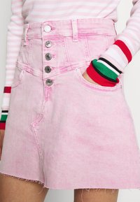 Lichtroze denim rok met hoge taille, vijfknops sluiting en een rafelig zoom. Voorzien van twee voorzakken en gestikte details.