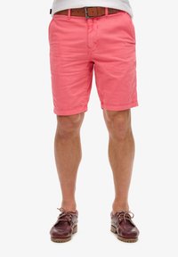 Pantalones cortos de algodón rosa con un frente plano, pasantes para cinturón y bolsillos laterales. Combinados con zapatos de barco de cuero marrón.