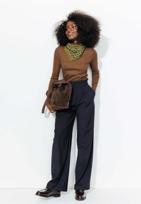 Tunique marron à manches longues, écharpe à motifs verts, pantalon large rayé bleu marine, sac en suedine marron et chaussures sombres brillantes.