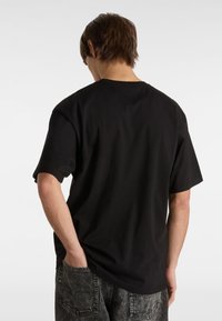 Black cotton t-shirt with a relaxed fit, short sleeves, and rounded neckline. Displayed from the back, showing smooth texture and minimal detailing.