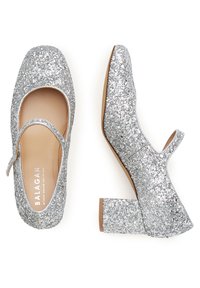 Tacones plateados brillantes con un diseño de Mary Jane, que presentan una puntera redonda, una correa en el empeine y un tacón cuadrado. Textura de purpurina en todo el calzado.