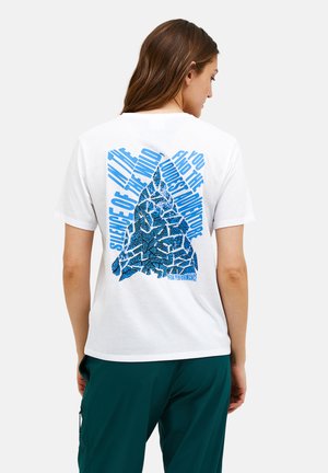 Kvinde iført en hvid t-shirt med en blå bjerggrafik og teksten "Stilhed i vildmarken, du afslutter det længste eventyr" på ryggen.