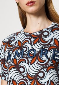 Brown and light blue patterned T-shirt featuring an embroidered "AMORE" in dark blue thread. Short sleeves and crew neckline.