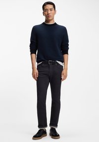 Suéter de punto azul marino oscuro con puños acanalados, jeans negros con bajos remangados y zapatillas negras con suela de goma. Diseño limpio y minimalista.