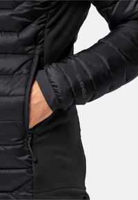 Sort isoleret jakke med en puffy tekstur, glat og strækbart sidepanel samt en lynlåslomme på venstre side.