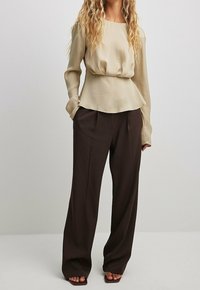 Blusa beige a maniche lunghe con vita arricciata, abbinata a pantaloni a gamba larga marrone scuro. Tessuto morbido con un design rilassato e fluido.