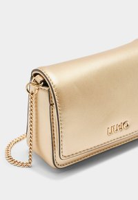 Borsa a spalla in pelle dorata con una superficie liscia, dotata di chiusura a patta e una tracolla a catena. Logo impresso sul fronte.