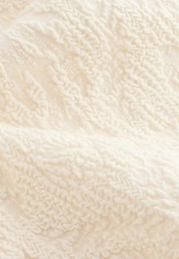 Texturerad vitt tyg med intrikata, upphöjda zickzackmönster. Mjukt och pluffigt material som följer en vågig design över ytan.