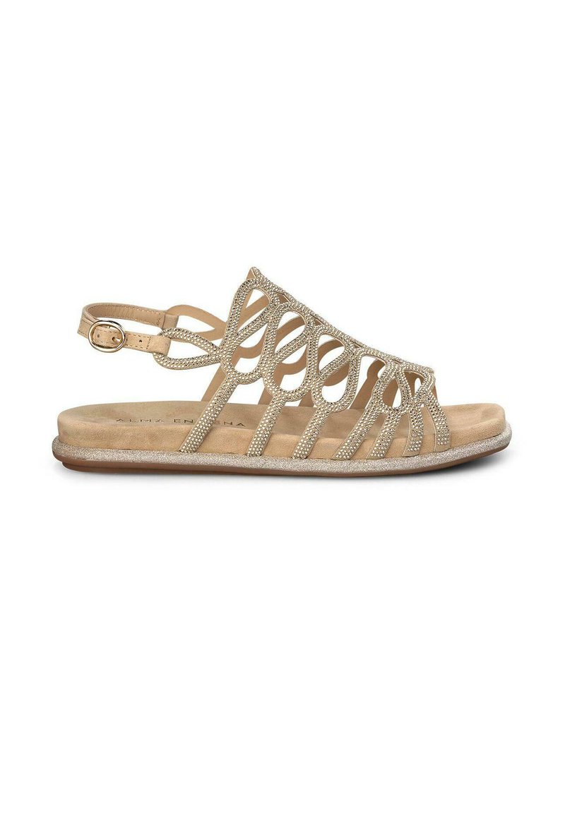 Beige sandaal met een ingewikkeld uitgesneden ontwerp, versierd met glinsterende accenten. Beschikt over een verstelbare enkelriem en een platte zool.